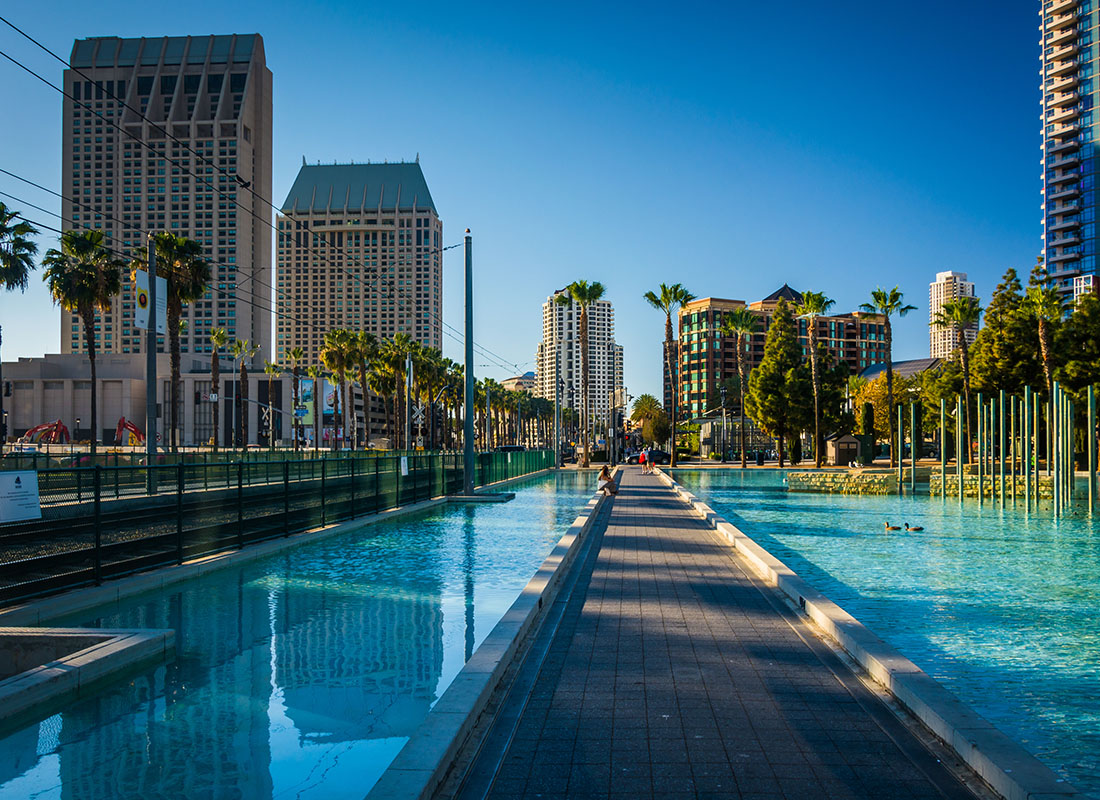 About Our Agency - Walkway with Pools on both Sides in a Childrens Park Surrounded by Palm Trees in Downtown San Diego California with Commercial Buildings in the Distance