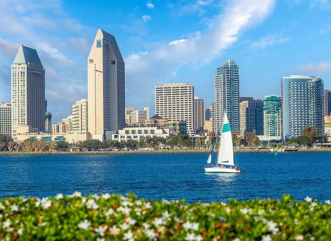 Read Our Reviews - Skyline View of Commercial Buildings in Downtown San Diego California with a Sailboat on the Water on a Sunny Day